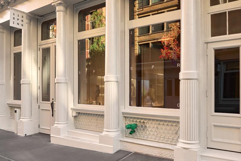 Exterior of 113 Spring, a white cast-iron SoHo building with large windows, fluted columns, and floral displays inside.